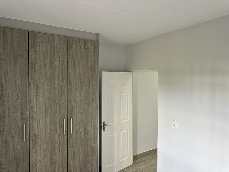 A clean, empty bedroom featuring modern wood-look built-in cupboards, neutral wall finishes, and tiled flooring.