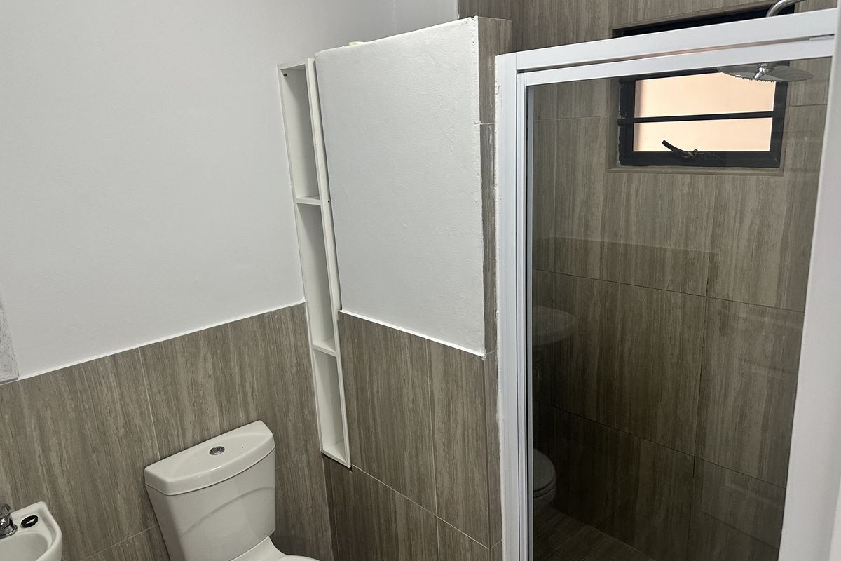 A functional bathroom featuring a shower enclosure, toilet, basin, and modern wood-look wall tiling with built-in shelving.