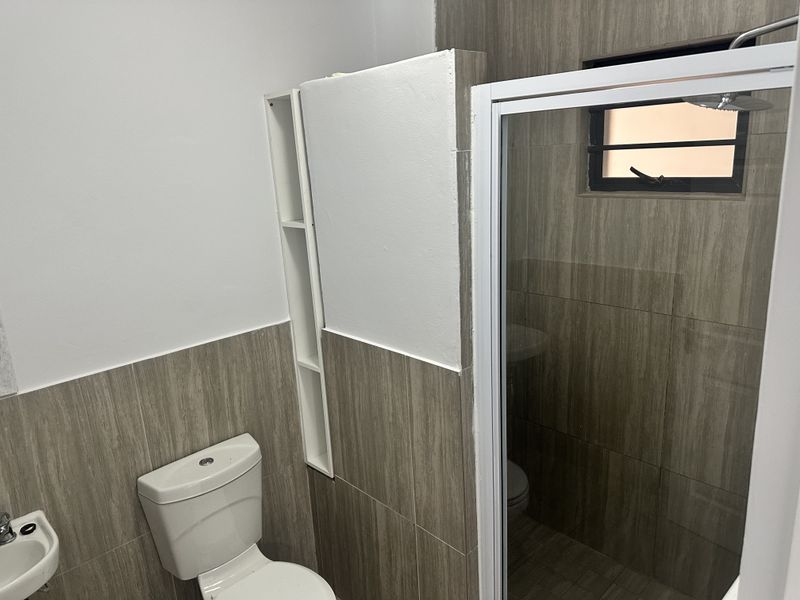 A functional bathroom featuring a shower enclosure, toilet, basin, and modern wood-look wall tiling with built-in shelving.