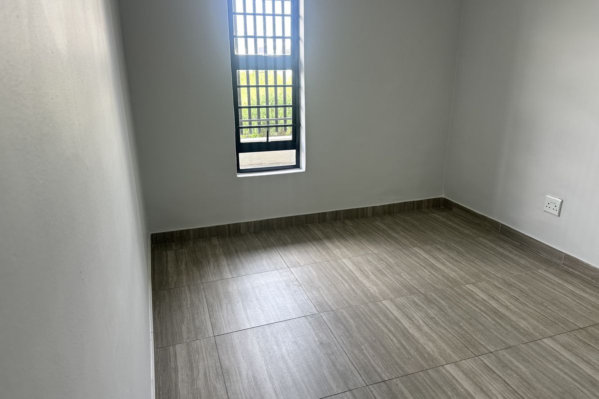 A clean, empty bedroom featuring modern wood-look floor tiles and a window fitted with security bars.