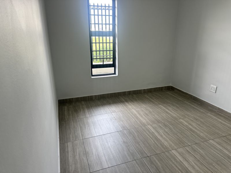 A clean, empty bedroom featuring modern wood-look floor tiles and a window fitted with security bars.