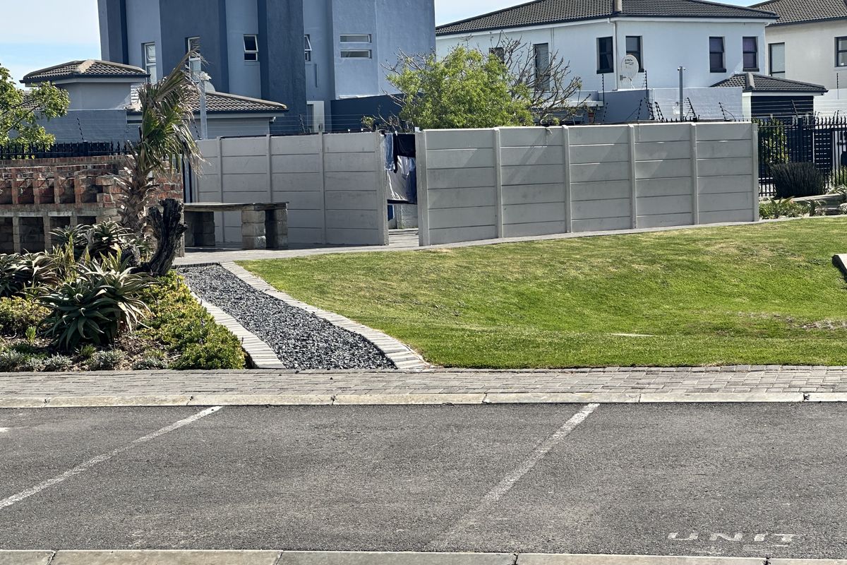 Rear garden area featuring a lawn, paved pathway, and a brick built-in braai, enclosed by a precast concrete boundary wall.