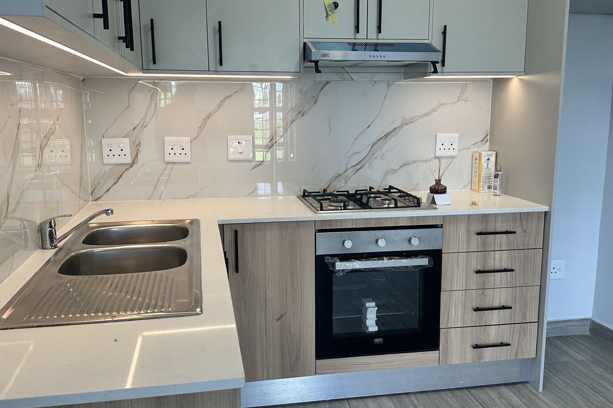 Modern kitchen featuring light wood cabinetry, quartz countertops, marble-look splashback, and integrated appliances including a gas hob and oven.