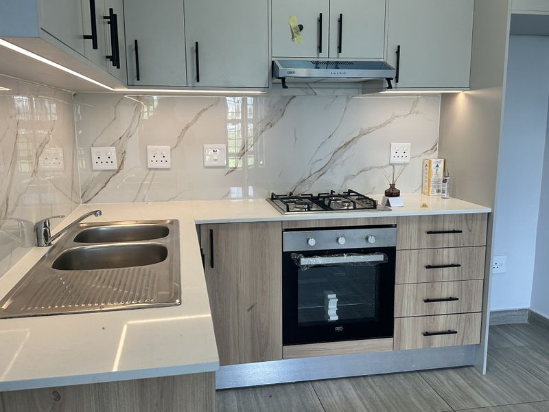 Modern kitchen featuring light wood cabinetry, quartz countertops, marble-look splashback, and integrated appliances including a gas hob and oven.