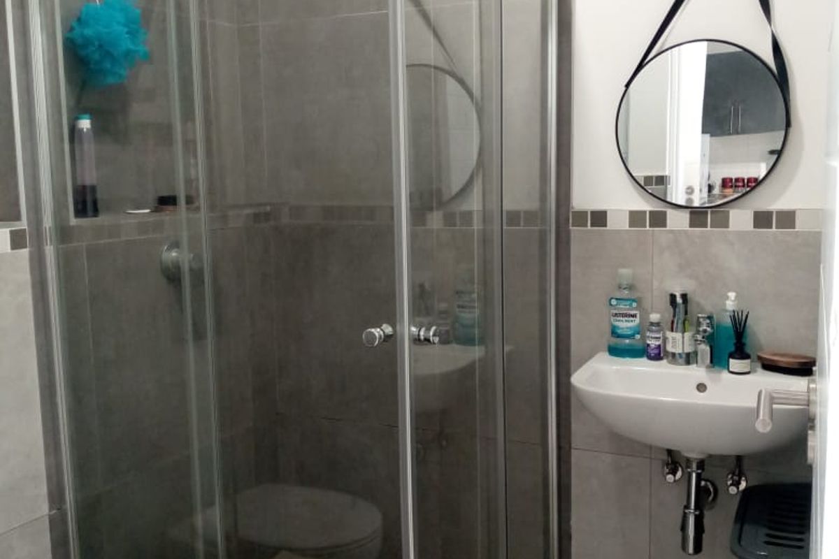 A functional bathroom featuring a glass-enclosed shower, wall-mounted basin, and neutral grey tiling throughout.