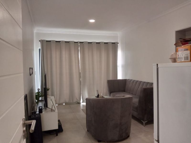 A well-lit living room featuring neutral tiled flooring, recessed ceiling lights, and a large sliding glass door providing access to the exterior.