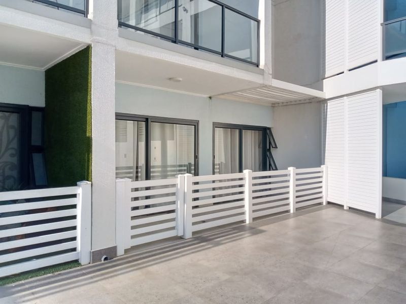 A modern, well-maintained ground floor patio featuring tiled flooring, a white slatted privacy fence, and direct access to the interior via sliding glass doors.