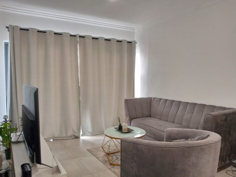 A well-lit living room featuring neutral tiled flooring and decorative cove cornicing, providing a clean and comfortable space.