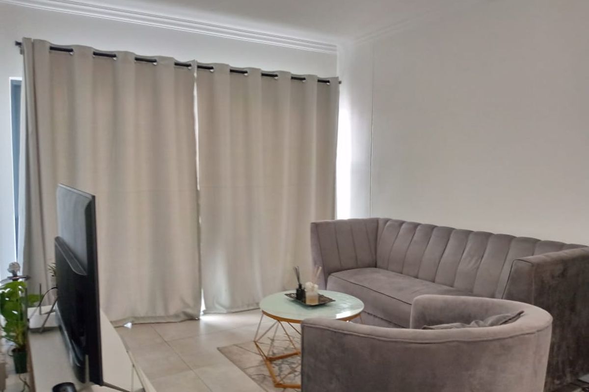 A well-lit living room featuring neutral tiled flooring and decorative cove cornicing, providing a clean and comfortable space.