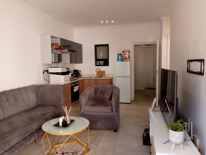 Open-plan living area featuring a compact kitchen with built-in cabinetry, oven, and extractor fan, seamlessly flowing into the lounge space with tiled flooring.