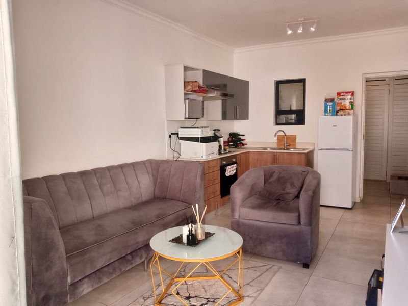 Open-plan living area featuring a compact kitchen with built-in cabinetry, oven, extractor fan, and tiled flooring throughout.