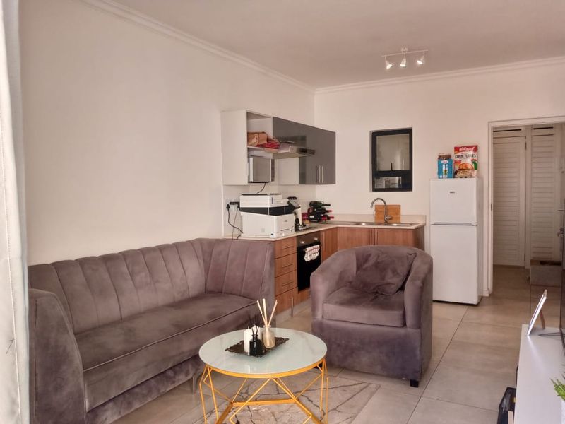 Open-plan living area featuring a compact kitchen with built-in cabinetry, oven, and extractor fan, seamlessly connected to the lounge space with tiled flooring.