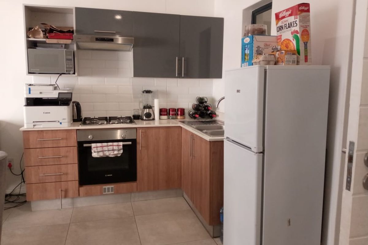 Compact kitchen featuring wood-finish lower cabinets, grey upper cabinets, gas hob, built-in oven, and a tiled backsplash.