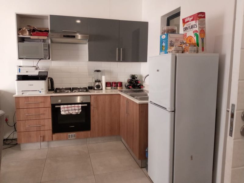 Compact kitchen featuring wood-finish lower cabinets, grey upper cabinets, gas hob, built-in oven, and a tiled backsplash.