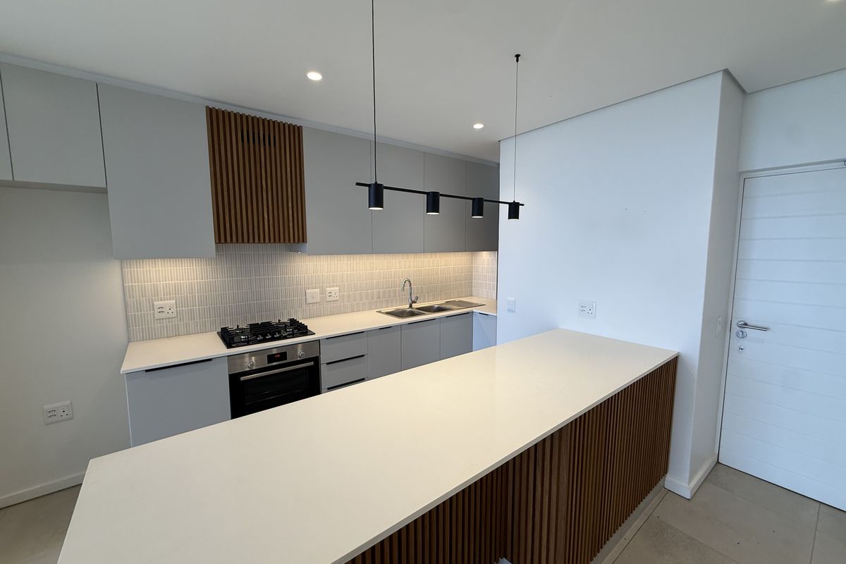 Modern kitchen featuring sleek cabinetry, stone countertops, a gas hob, built-in oven, and stylish slatted timber accents on the island and extractor housing.