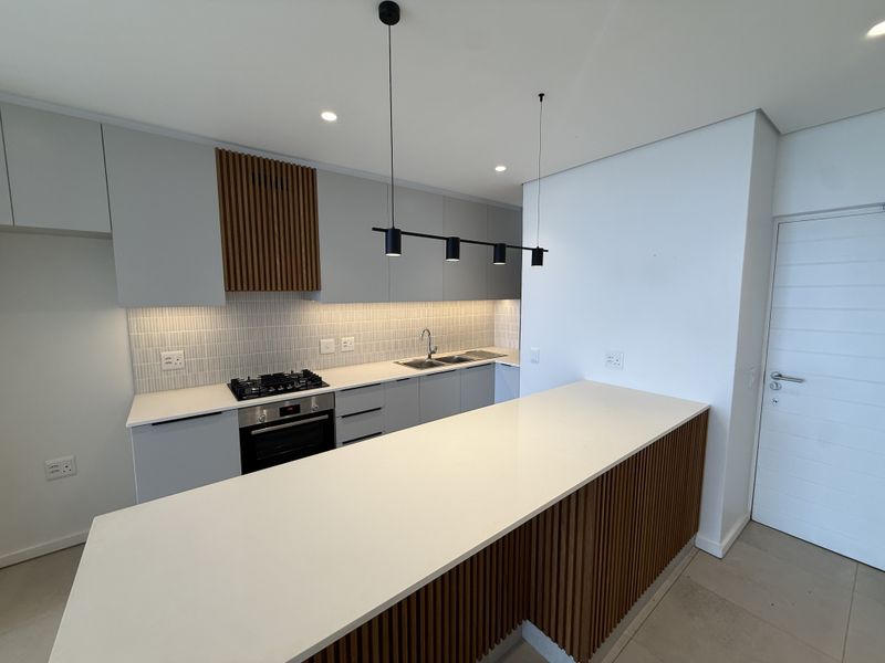 Modern kitchen featuring sleek cabinetry, stone countertops, a gas hob, built-in oven, and stylish slatted timber accents on the island and extractor housing.