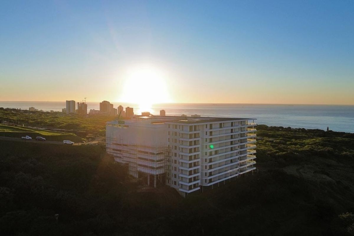 Aerial view of a multi-story apartment building under construction, situated in a coastal landscape at sunset.