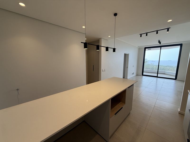 Modern open-plan living area featuring a sleek kitchen island with quartz countertops, recessed lighting, and large sliding doors leading to a balcony with views.