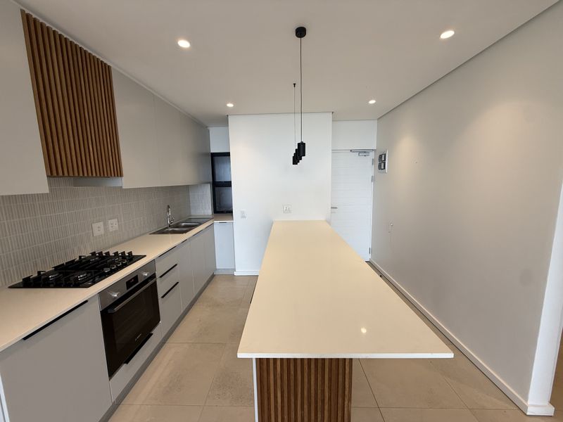 Modern kitchen featuring sleek cabinetry, stone countertops, a gas hob, built-in oven, and a central island with decorative wood detailing.