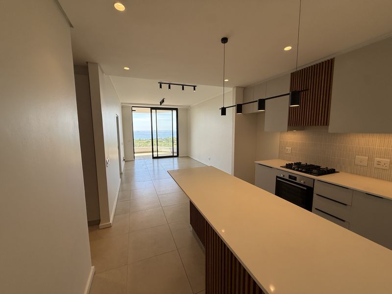 Modern open-plan kitchen and living area featuring a central island, sleek cabinetry, and sliding doors leading to a balcony with ocean views.