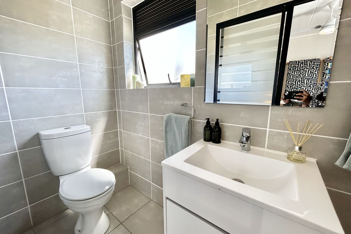A modern bathroom featuring neutral wall and floor tiles, a white vanity with basin, and a wall-mounted mirror.