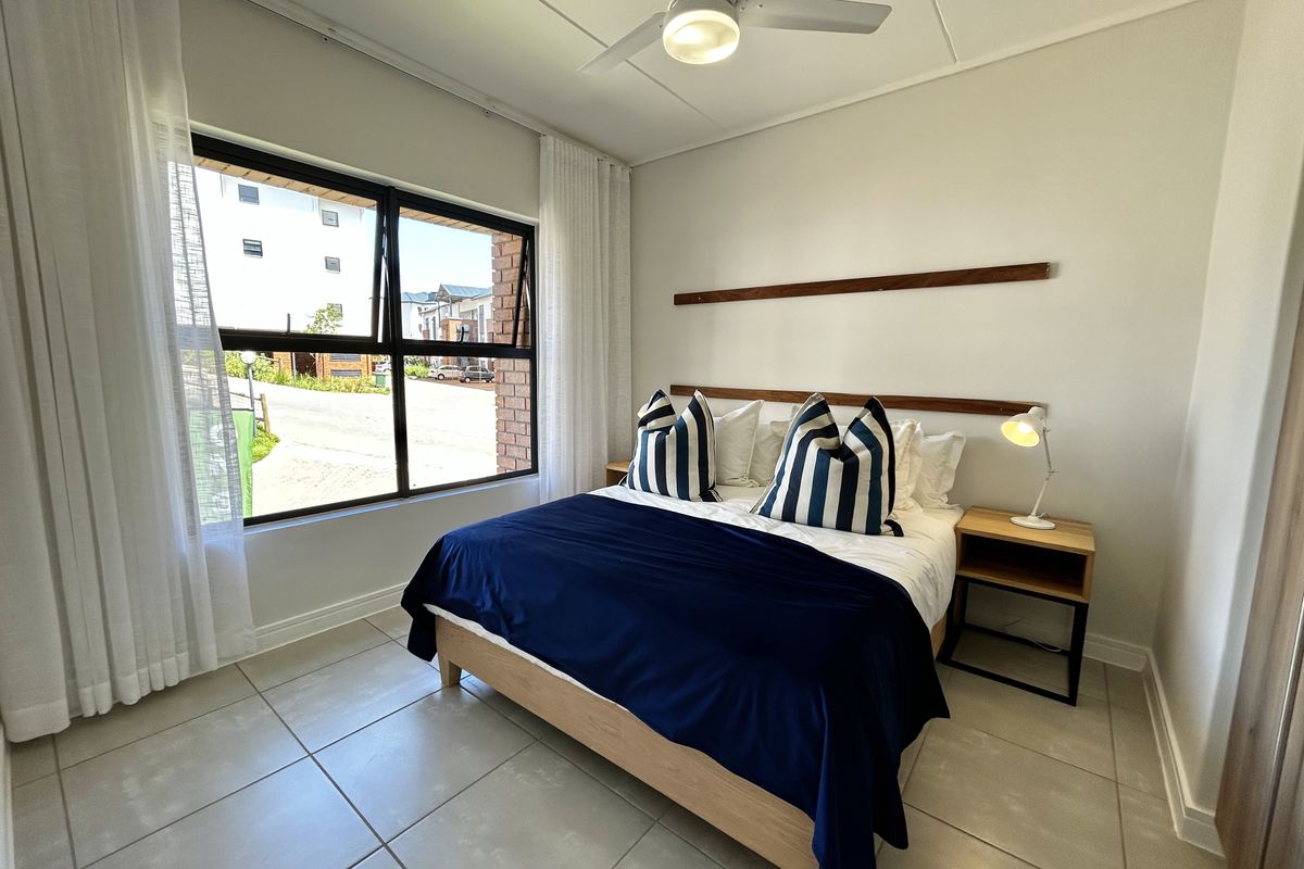 A well-maintained bedroom featuring neutral tiled flooring, a modern ceiling fan, and large aluminium-framed windows providing natural light.