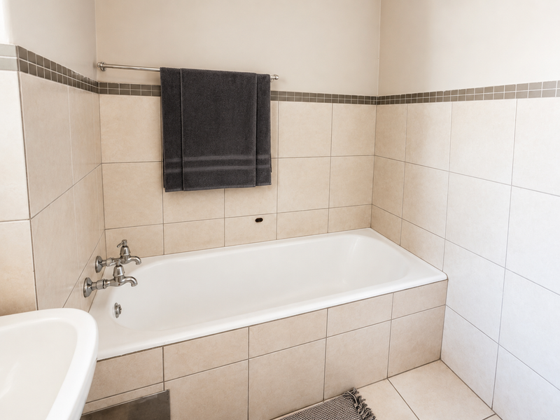 A clean, functional bathroom featuring a built-in bathtub with chrome fixtures and neutral wall and floor tiling.