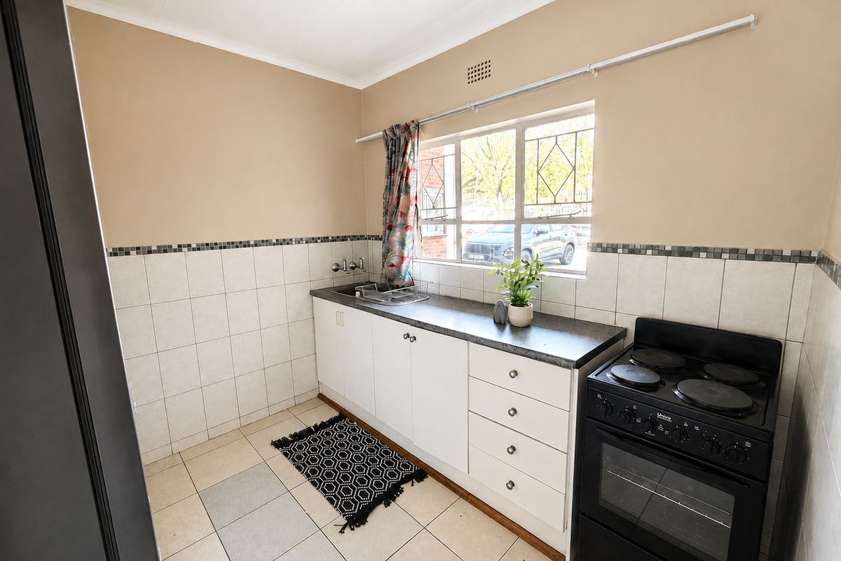 A functional kitchen featuring white cabinetry, a dark laminate countertop, tiled backsplash, and a freestanding electric stove with security-barred window.