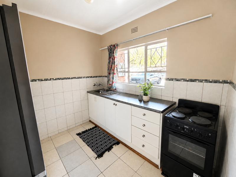 A functional kitchen featuring white cabinetry, a dark laminate countertop, tiled backsplash, and a freestanding electric stove with security-barred window.