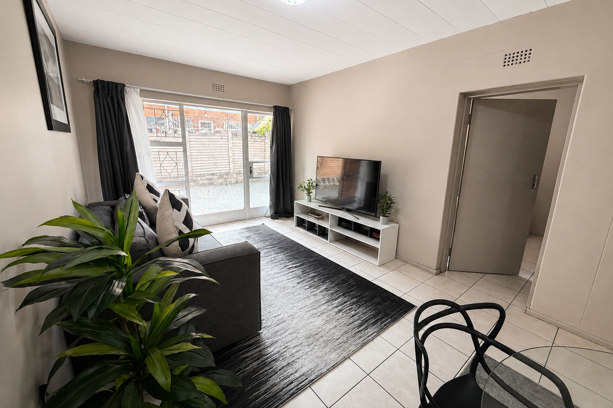 A bright living room featuring neutral walls, tiled flooring, and a large sliding glass door providing natural light and access to the exterior.