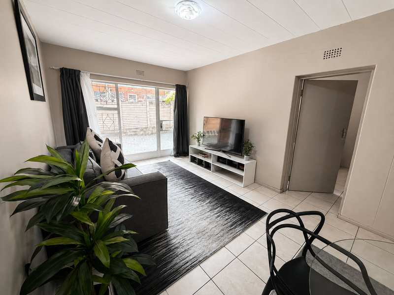 A bright living room featuring neutral walls, tiled flooring, and a large sliding glass door providing natural light and access to the exterior.