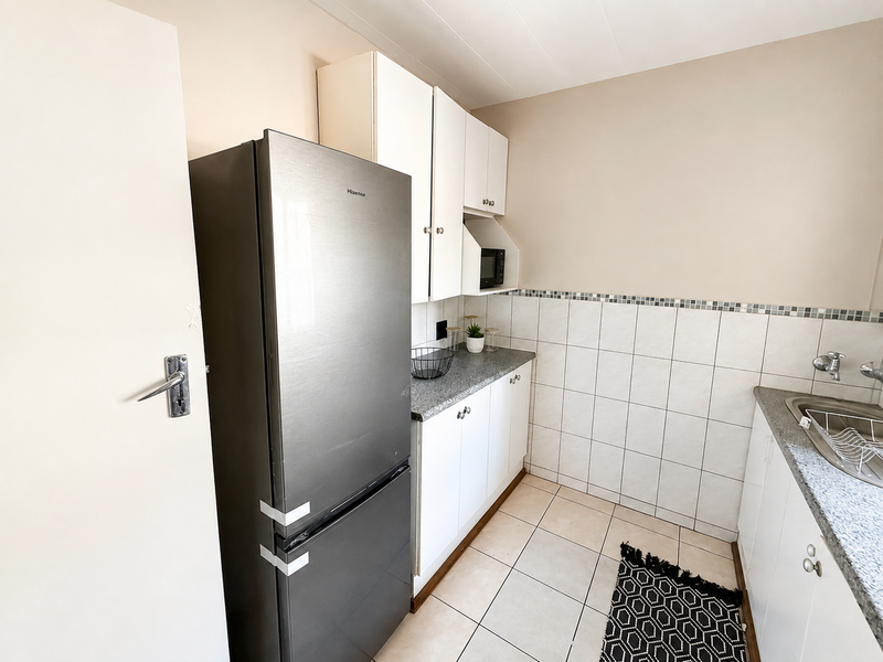 A functional kitchen featuring white cabinetry, laminate countertops, tiled backsplash, and tiled flooring, providing a clean and practical workspace.