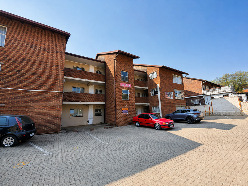 Exterior view of the Agatha apartment complex featuring a face brick facade, paved parking area, and multi-level residential units with balconies.