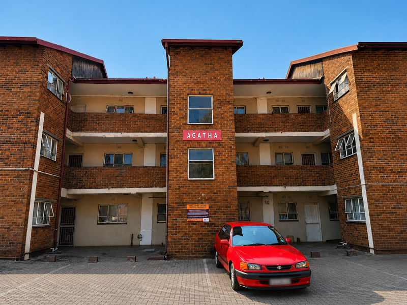 Front elevation of Agatha apartment complex featuring a multi-story brick facade with paved parking area and balcony access.