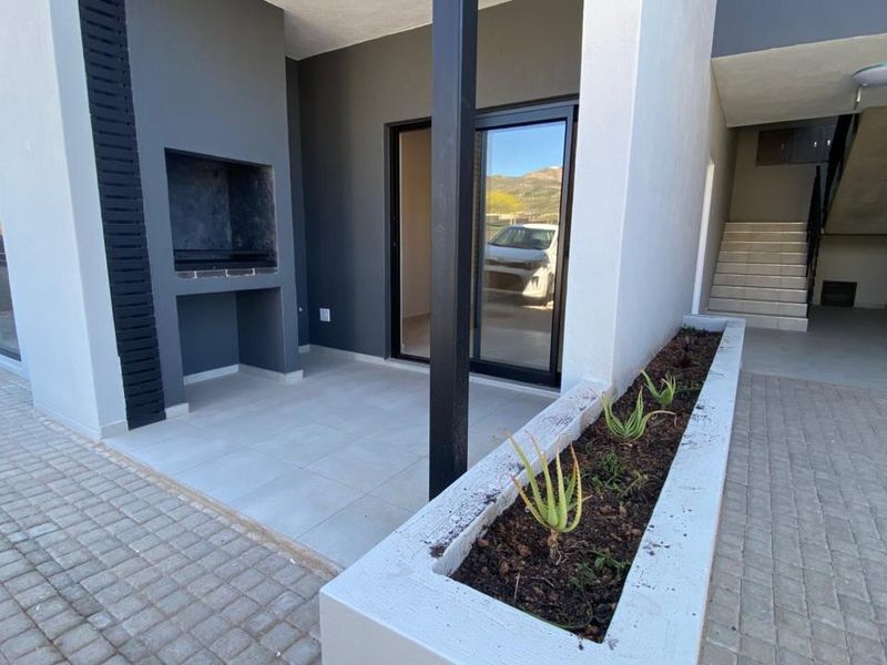 A modern covered patio featuring a built-in braai, tiled flooring, and an integrated concrete planter box, providing a functional outdoor entertainment space.