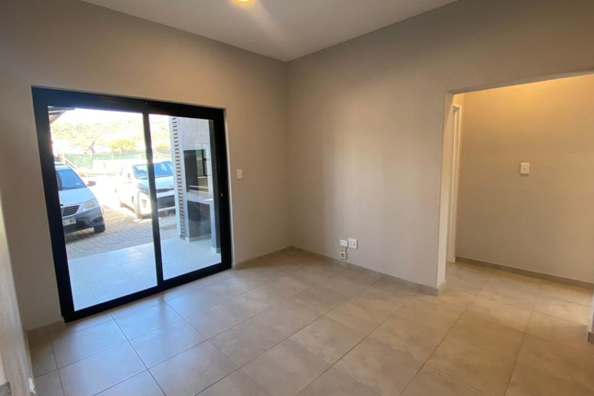 An empty, neutrally painted living area featuring tiled flooring and a large sliding glass door providing access to an outdoor patio space.