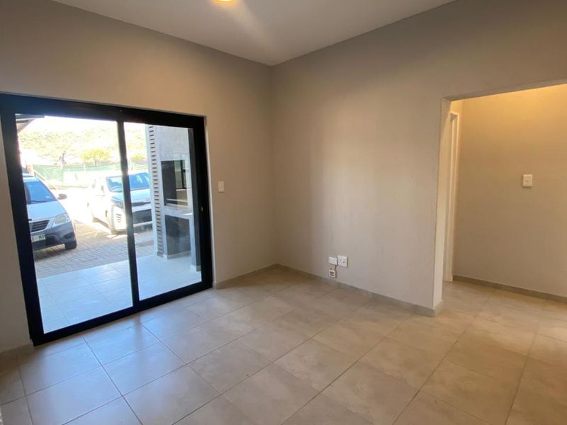 An empty, neutrally painted living area featuring tiled flooring and a large sliding glass door providing access to an outdoor patio space.