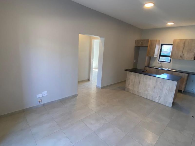 An open-plan living and kitchen area featuring modern wood-finish cabinetry, dark stone countertops, and neutral tiled flooring throughout.