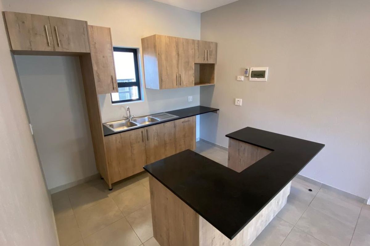 Modern kitchen featuring light wood-look cabinetry, dark countertops, a stainless steel double sink, and neutral tiled flooring in an open-plan layout.