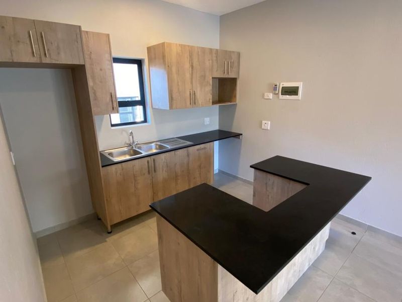 Modern kitchen featuring light wood-look cabinetry, dark countertops, a stainless steel double sink, and neutral tiled flooring in an open-plan layout.
