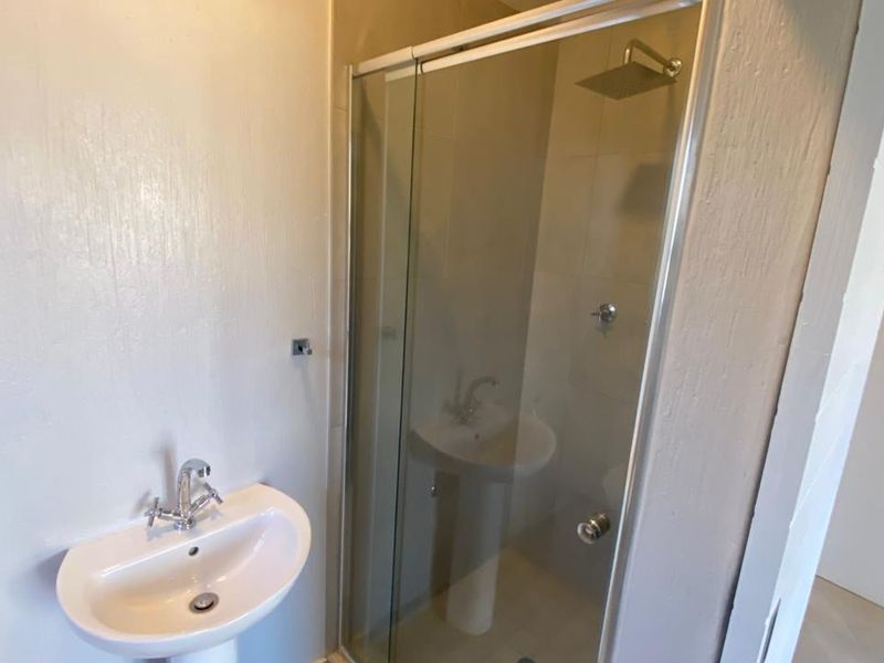 A clean, modern bathroom featuring a pedestal basin with chrome mixer tap and a glass-enclosed shower with a fixed overhead shower rose.