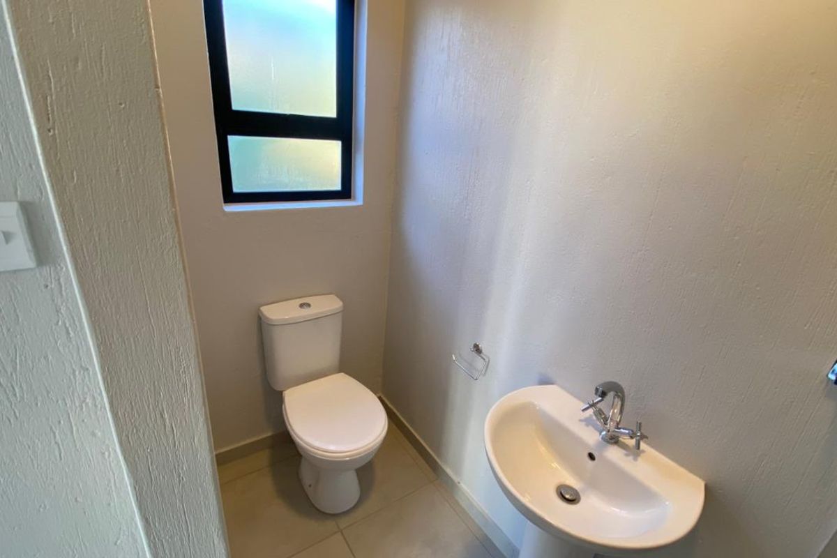 A clean and functional guest bathroom featuring a white pedestal basin, modern mixer tap, and a standard toilet with tiled flooring.