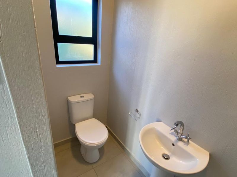 A clean and functional guest bathroom featuring a white pedestal basin, modern mixer tap, and a standard toilet with tiled flooring.