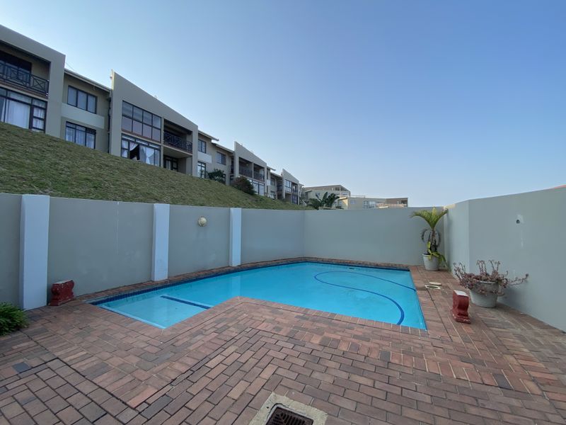 Private swimming pool area featuring brick paving and a surrounding boundary wall, set against the backdrop of the apartment complex.