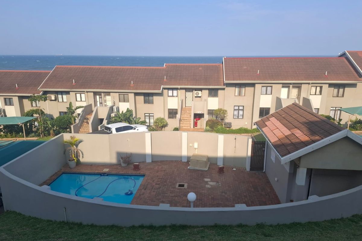 Aerial view of a residential apartment complex featuring a private swimming pool, paved courtyard, and ocean views.