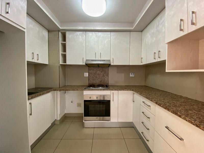 A clean, functional kitchen featuring white cabinetry, granite-look laminate countertops, built-in oven, electric hob, and extractor fan with neutral floor tiling.