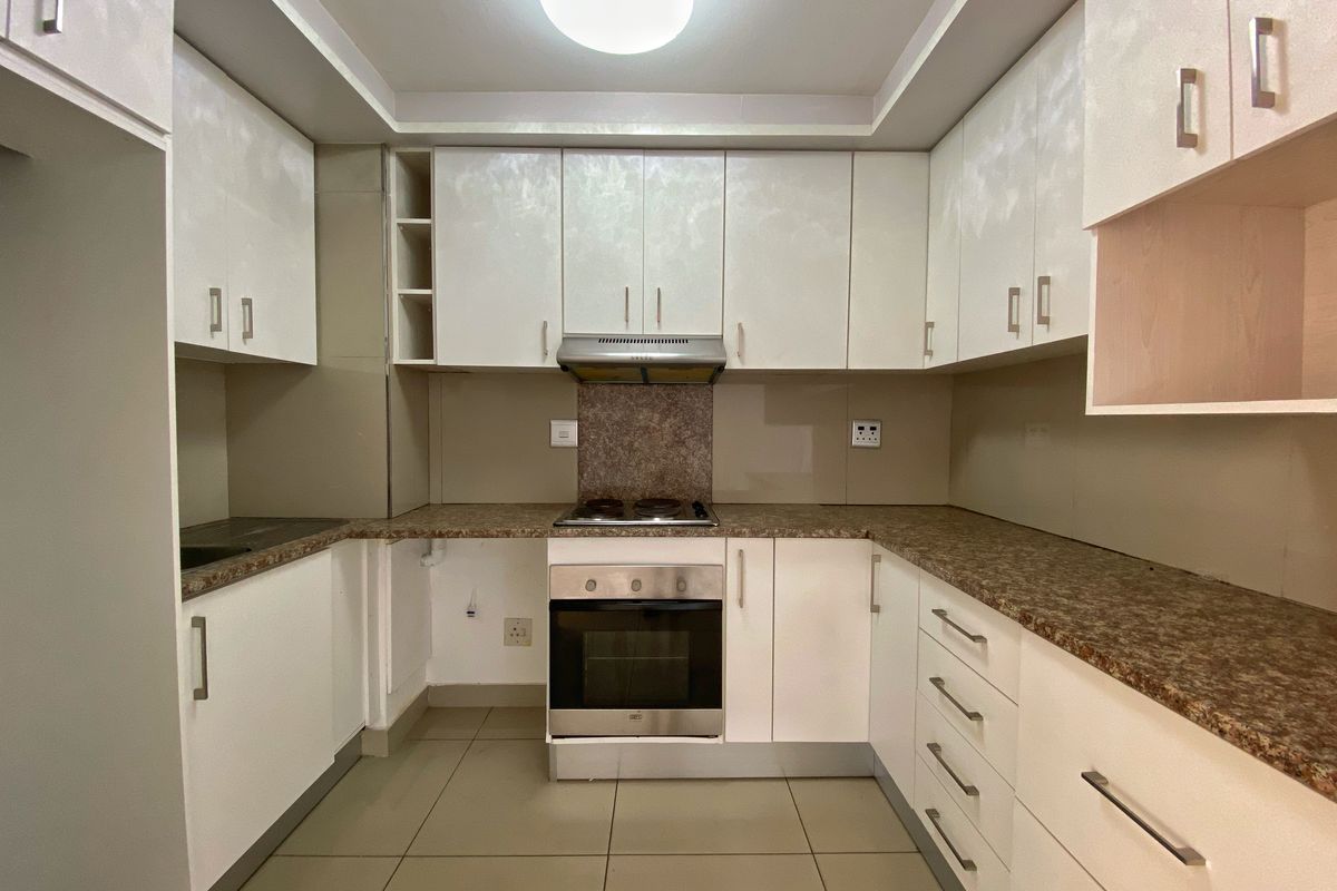 A clean, functional kitchen featuring white cabinetry, granite-look laminate countertops, built-in oven, electric hob, and extractor fan with neutral floor tiling.