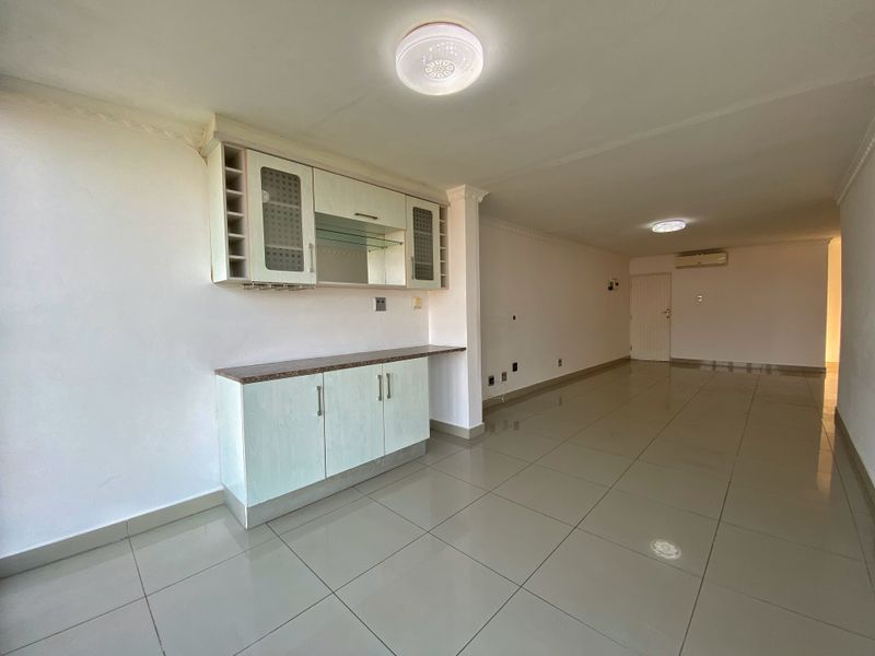 Spacious open-plan living area featuring neutral tiled flooring, built-in cabinetry with stone countertop, and split-system air conditioning in a well-lit, vacant space.