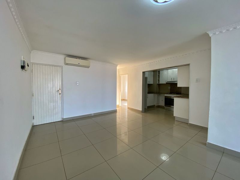 An open-plan living area featuring tiled flooring, a split-system air conditioner, and a functional kitchen with built-in cabinetry and appliances.