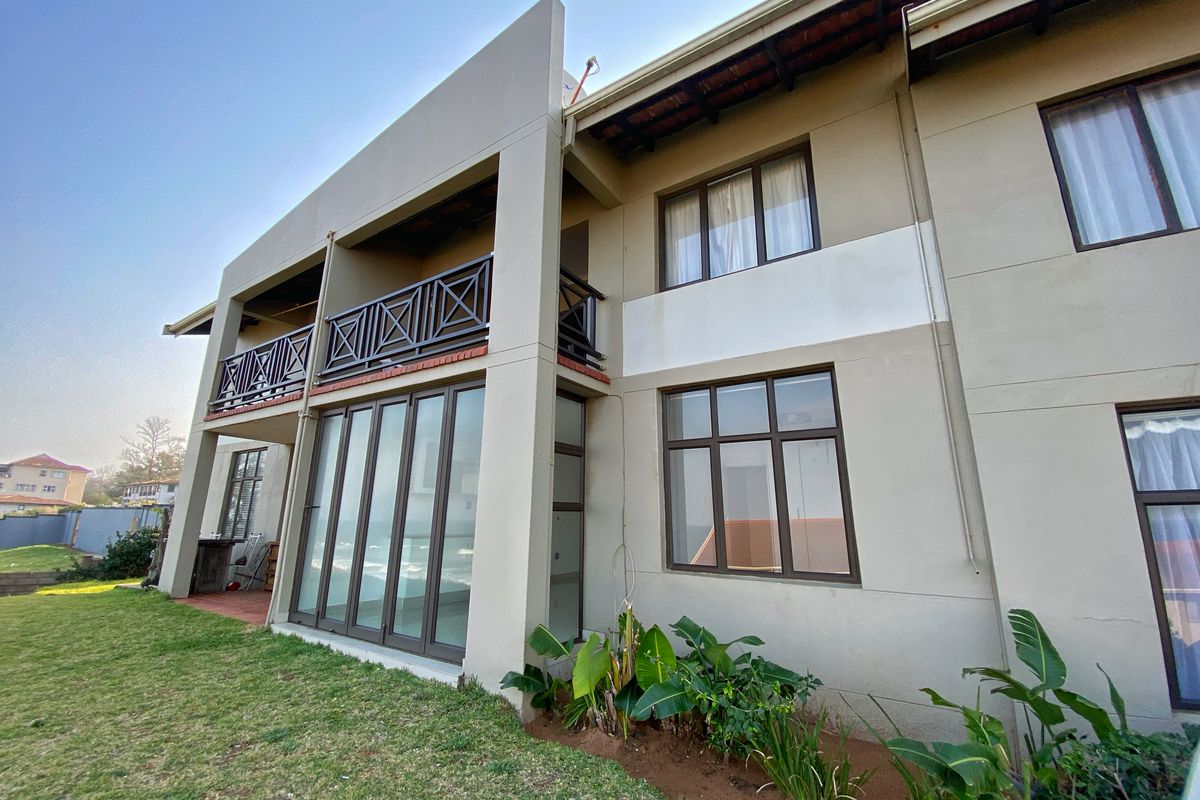Rear elevation of the apartment building featuring a balcony, large sliding glass doors, and established garden area.